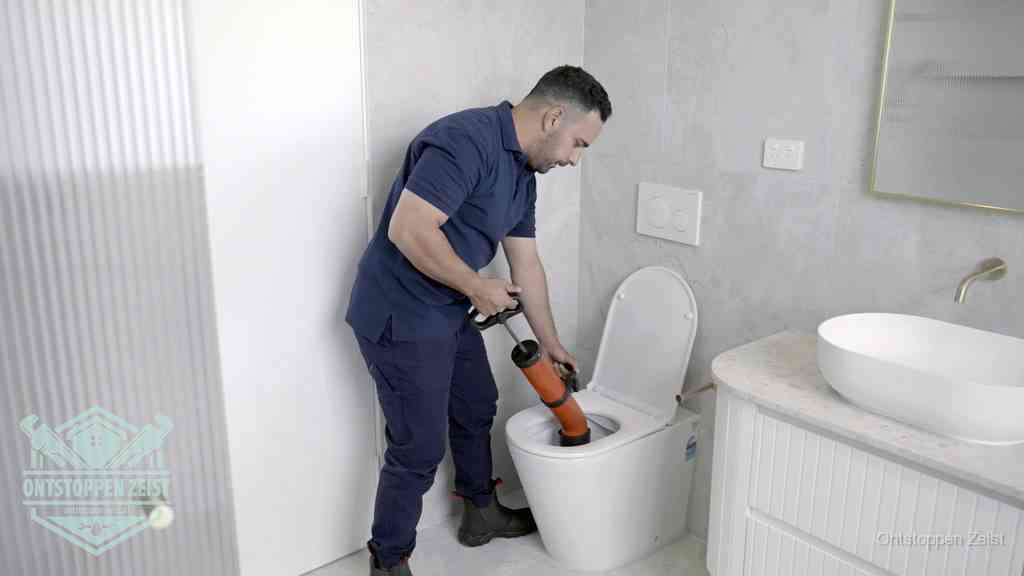Een monteur buigt over een wandcloset en duwt met de hand een persluchtontstopper in de toiletpot om de verstopping handmatig los te maken in Zeist Een monteur buigt over een wandcloset en duwt met de hand een persluchtontstopper in de toiletpot om de verstopping handmatig los te maken in Zeist
