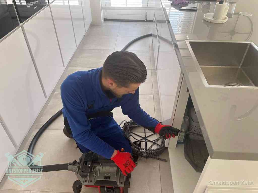 Een monteur ontstopt de keukenafvoer onder de spoelbak met een elektrische veermachine in Zeist Een monteur ontstopt de keukenafvoer onder de spoelbak met een elektrische veermachine in Zeist