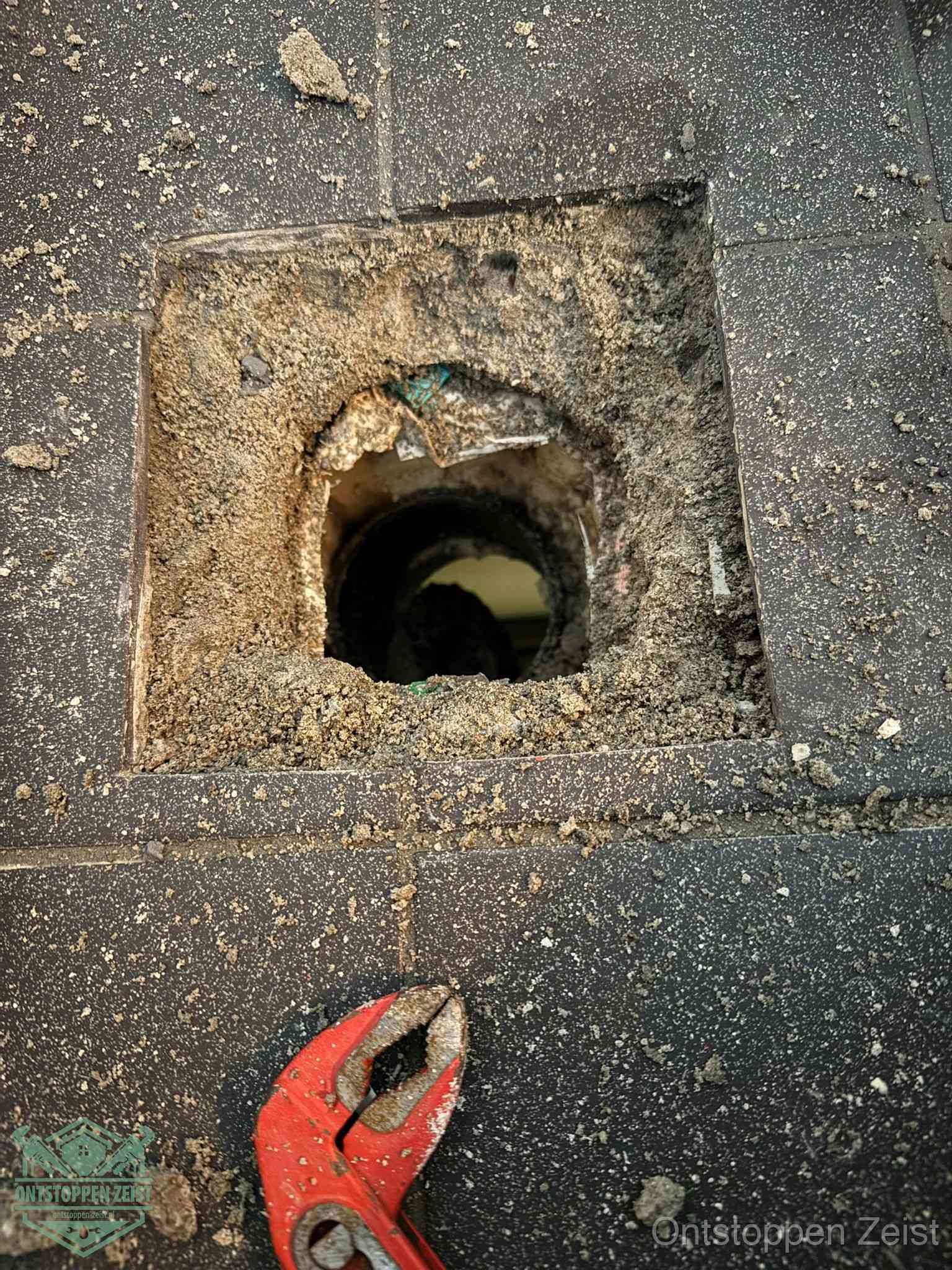 Een geopend rioolputje in een betontegelvloer met losgemaakt rooster en een zichtbare ronde afvoerbuis, het achterhalen waar de afvoerverstopping zit in Zeist