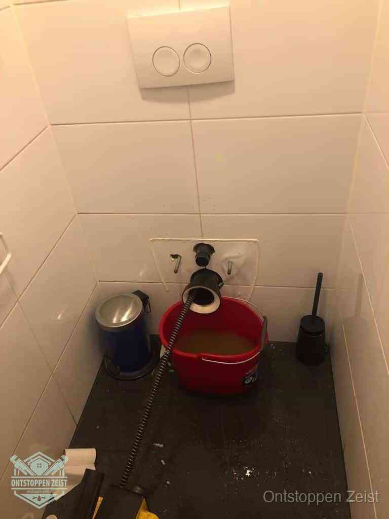 Een ontstopte wand-wc met verwijderde toiletpot waar een ontstoppingsveer in de wanduitgang verdwijnt, het achterhalen waar de verstopping zit in Zeist Een ontstopte wand-wc met verwijderde toiletpot waar een ontstoppingsveer in de wanduitgang verdwijnt, het achterhalen waar de verstopping zit in Zeist