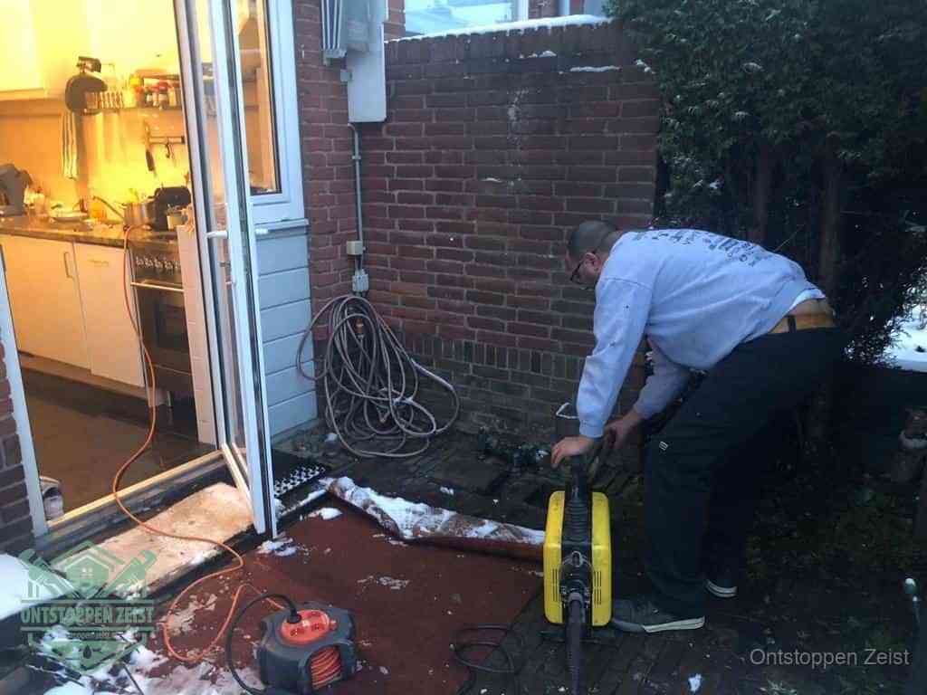 Een monteur werkt buiten bij een open riool-/grondput met een elektrische ontstoppingsmachine om een verborgen afvoerprobleem op te sporen in Zeist