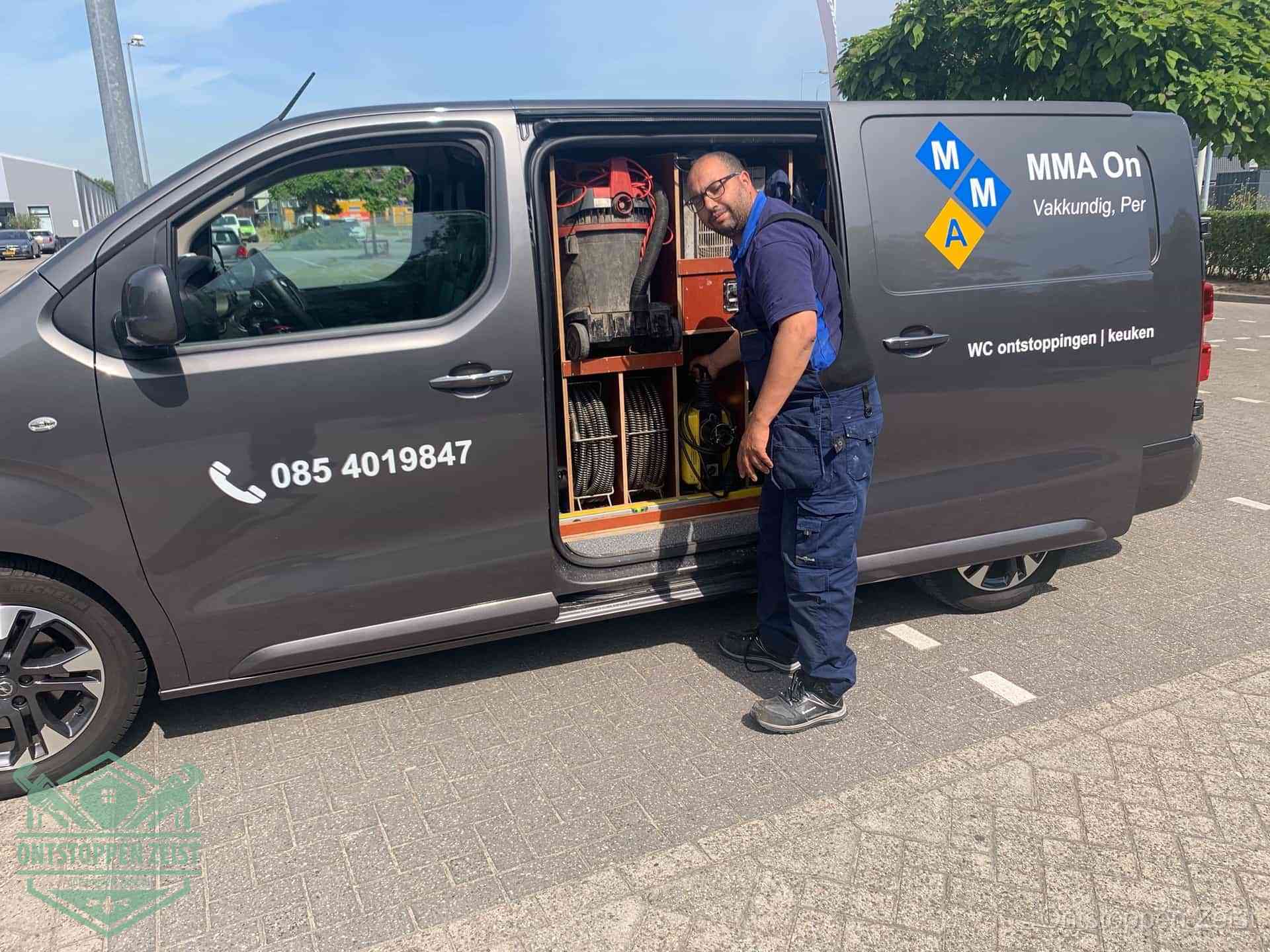 Een monteur bij de open schuifdeur van zijn bedrijfsbus op een parkeerplaats, klaar om de oorzaak van terugkerende afvoerverstoppingen aan te pakken in Zeist