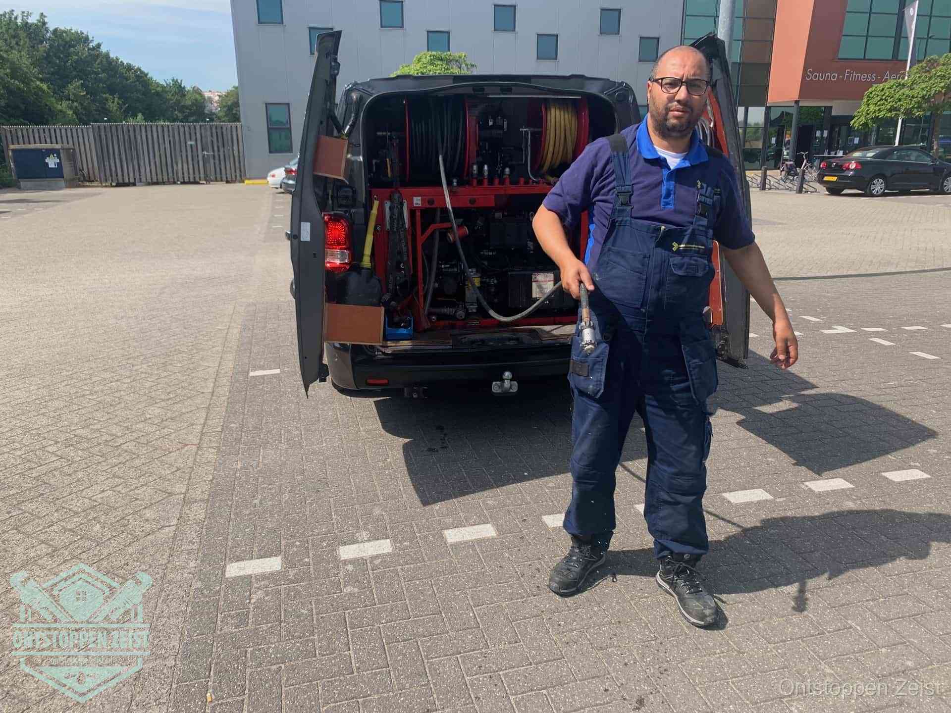 Een monteur bij zijn bestelbus met een hogedruk- en rioolreinigingsunit, klaar om de oorzaak van terugkerende wc-verstoppingen aan te pakken in Zeist Een monteur bij zijn bestelbus met een hogedruk- en rioolreinigingsunit, klaar om de oorzaak van terugkerende wc-verstoppingen aan te pakken in Zeist