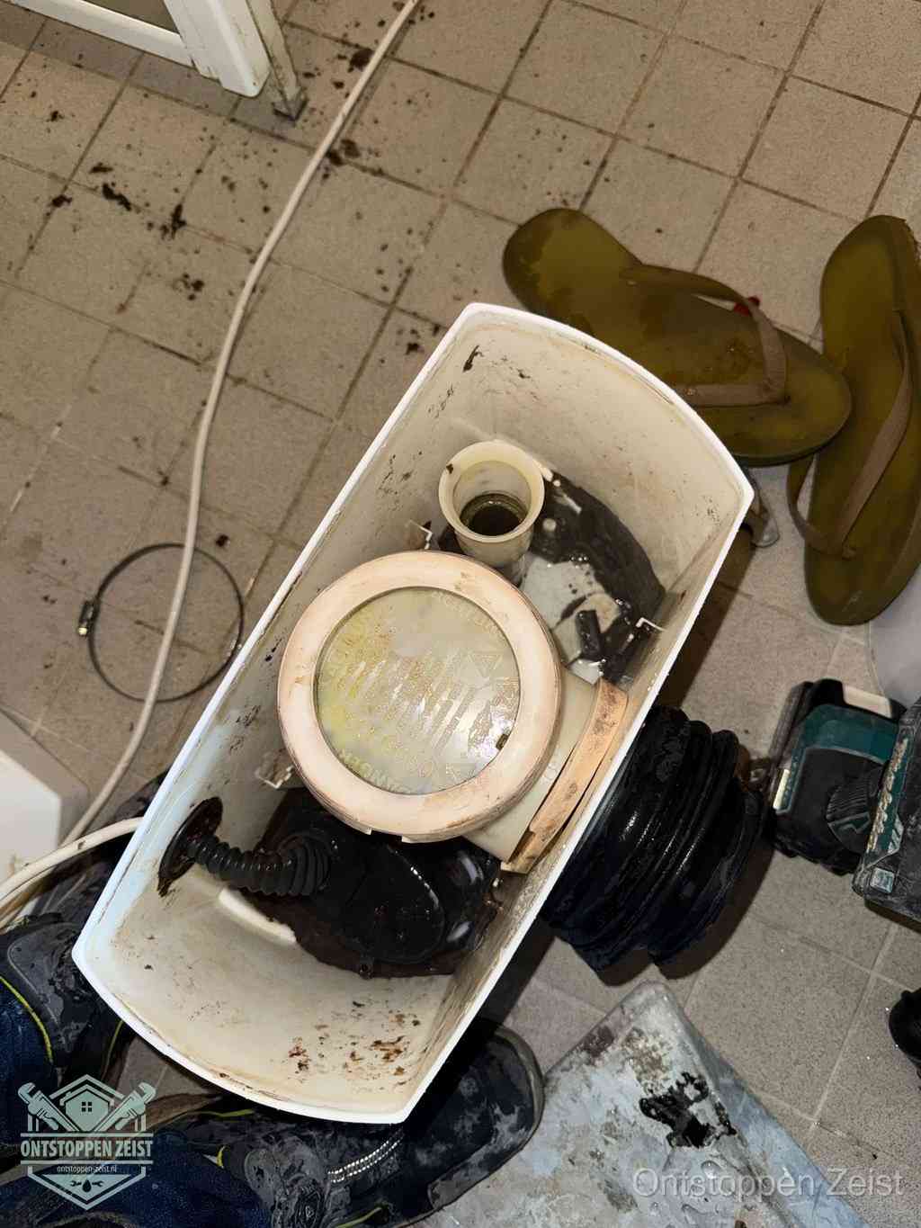 Een gedemonteerde toiletpot op de vloer met ontstoppingsveer en gereedschap ernaast, het verwijderen van een vastzittend voorwerp uit de wc in Zeist Een gedemonteerde toiletpot op de vloer met ontstoppingsveer en gereedschap ernaast, het verwijderen van een vastzittend voorwerp uit de wc in Zeist