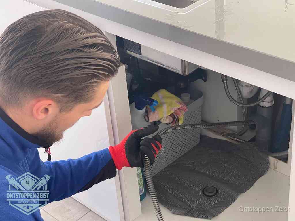 Een monteur voert een flexibele ontstoppingsveer in de afvoer om een verstopping voorbij de bocht van het toilet te bereiken in Zeist Een monteur voert een flexibele ontstoppingsveer in de afvoer om een verstopping voorbij de bocht van het toilet te bereiken in Zeist