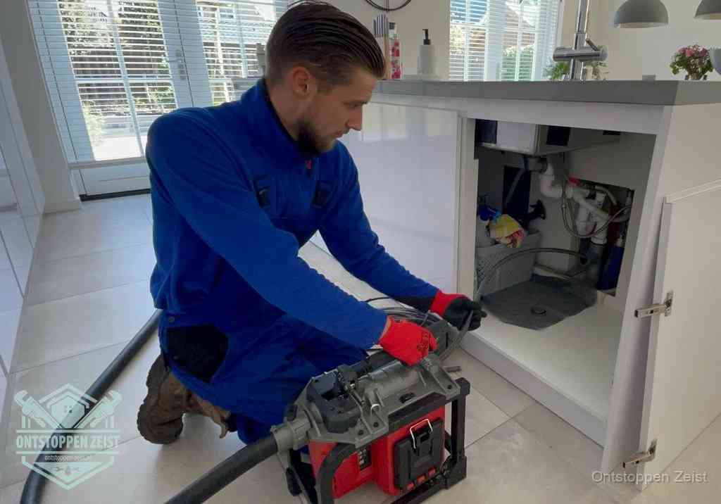 Een monteur voert een professionele elektrische ontstoppingsmachine in de afvoer onder de spoelbak tijdens het gootsteen ontstoppen in Zeist Een monteur voert een professionele elektrische ontstoppingsmachine in de afvoer onder de spoelbak tijdens het gootsteen ontstoppen in Zeist